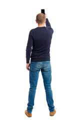 back view of standing young man and using a mobile phone. watching. Rear view people collection. backside view of person. Isolated over white background. A guy in a black sweater photographs on your