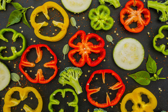 Fresh and raw slices of peppers, broccoli and zucchini on a black background.