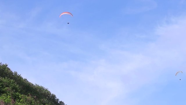 Paragliders fly over amazing mountain near the beach, Bali island, Indonesia. Beautiful view, sky and mountain full of plants. Full HD, 50 fps, 1080p.