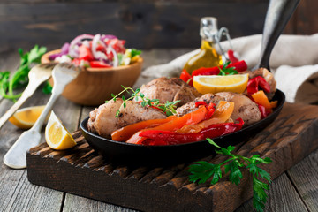 Chicken drumsticks with baked pepper and lemon in a frying pan on a dark background. Selective focus.
