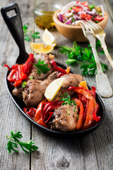 Chicken drumsticks with baked pepper and lemon in a frying pan on a dark background. Selective focus.