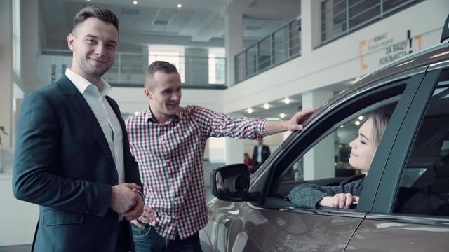 Unrecognizable Sales Manager Gives the Client the Keys from the Car. Then smiling woman customer look straight at the camera