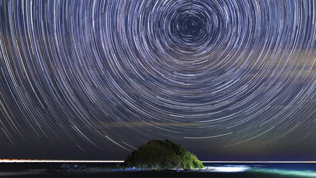 Majestic spiral star trails over ocean with island.
