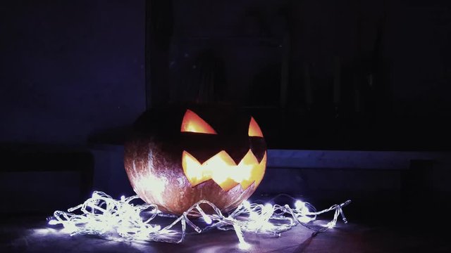 Halloween Jack o lantern with burning candle inside lay upon a white lights garland dark kitchen 4k