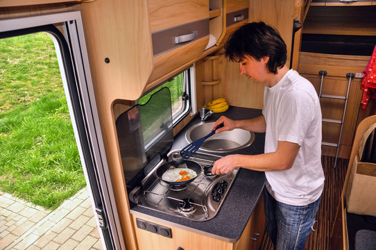 Family vacation, RV holiday trip, man cooking in camper. Motorhome interior

