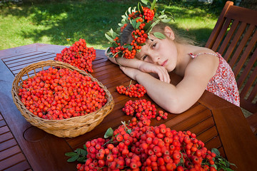 Sleeping young girl with a garland on his head made from rowan fruit. On the table, a wicker basket full of fruits rowan.