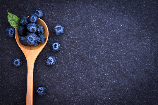  fresh picked blueberries in wooden spoon on black stone background
