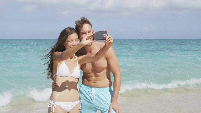 Attractive young Asian Caucasian couple portrait having fun in swimwear on beach smiling happy to camera taking selfie selfportrait for social media. RED EPIC SLOW MOTION 96 FPS.