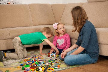 Children and their mother are playing with blocks on the ground