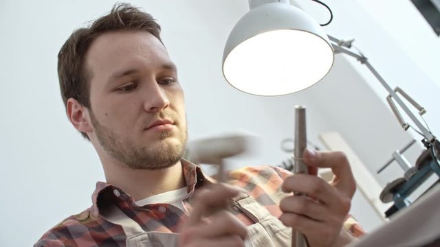 Low angle view of young jeweler hammering silver ring on steel mandrel while working in workshop