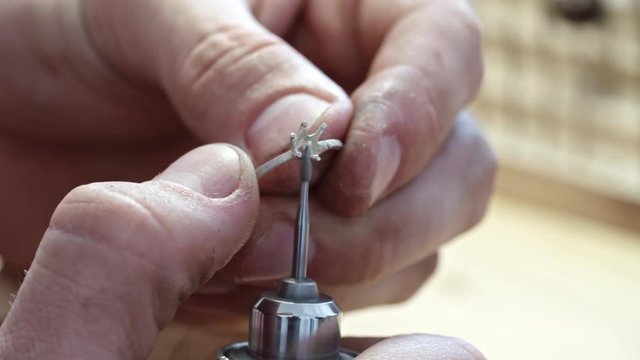 Closeup of male hands polishing claws of silver ring prong setting with jewel tool