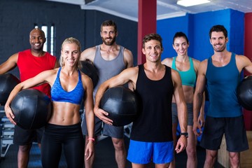 Fototapeta na wymiar Portrait of smiling friends holding exercise ball in gym