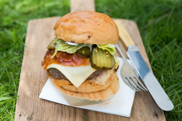 large burger on wooden board with knife and fork