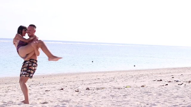 Young man holds and turns his sexy girlfriend on the beach of Bali island, Indonesia. Scene of couple playing on the tropical beach. Happy young guys swirling. Slow motion.