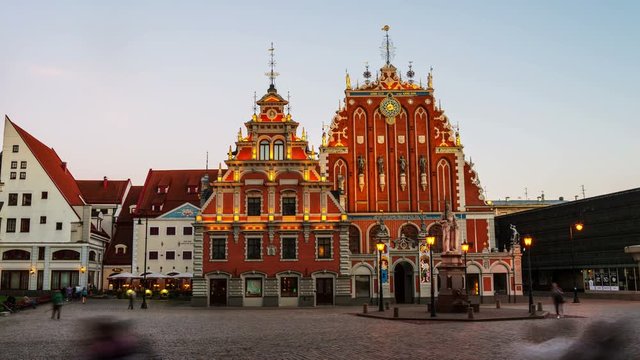 Illuminated House of the Blackheads in the old town of Riga, Latvia. Unidentified blurred people walking by the square. Time-lapse at sunset