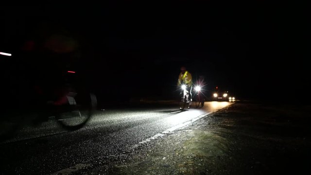 A  group of cycling athletes out on a long distance ride in the middle of the night with support vehicles.