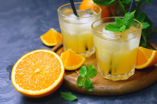 fresh organic orange juice in glass with ice and mint leaf decorated by cut orange fruits on wooden tray.