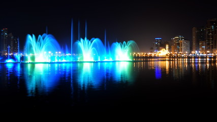 Colorful dancing fountain with mosque in the city at night with lively music, Sharjah, United Arab Emirates