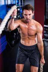 Fototapeta na wymiar Shirtless man holding rope in gym