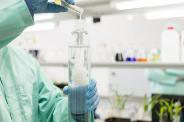 Lab technician pours liquid in high flask.