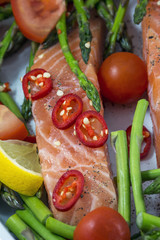 One piece of salmon with green asparagus, tomato and red pepper