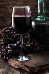Glass of red wine, served with grapes on a wooden background