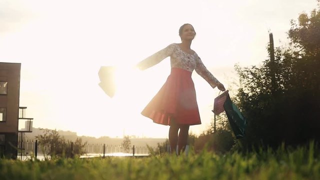 Shopaholic woman in beautiful dress spinning around holding many shopping bags walking on the street through the sun during sunset in slowmotion. 1920x1080