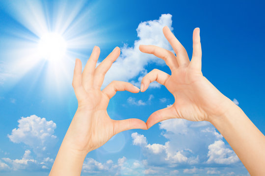 Showing Hands in the shape of heart against the blue sky with the sun. Sky background