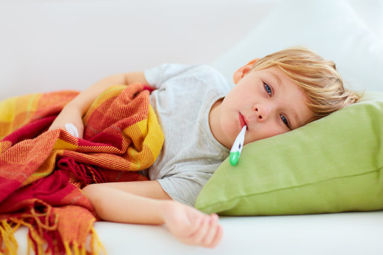 sick kid with runny nose and fever heat lying on couch at home