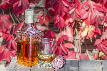 Bottle with glass tequila and sausage on table in garden