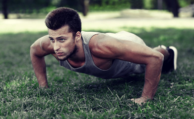 young man doing push ups on grass in summer park