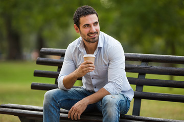 Young businessman is drinking coffee and resting from work at the park.
