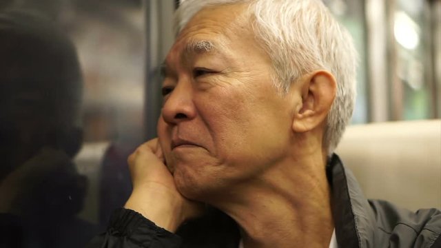 Senior Asian man sitting on train and looking out through window. Thinking and enjoying view during retirement trip