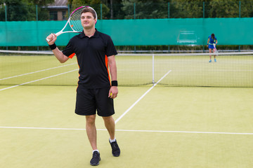 Happy male tennis player holding a racket on his shoulder after