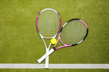 Two new pink tennis rackets with a tennis ball on a green grass