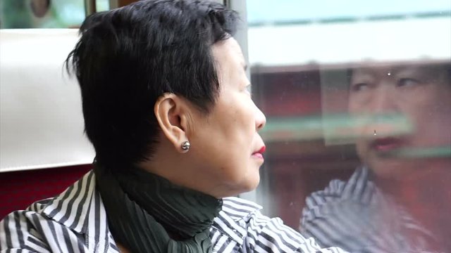 Senior Asian woman sitting on train and looking out through window. Thinking and enjoying view during retirement trip