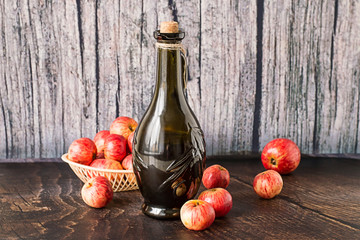 Bottle with wine and apples.   Glass bottle with wine and red ripe apples on an old wooden table.