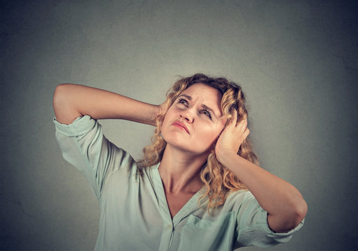annoyed, unhappy, stressed woman covering her ears, looking up