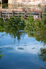 Spiegelung im Teich von Menschen, die einen Fußgängerüberweg auf einer Steinbrücke überqueren