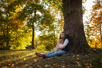 Cute Teenager girlsitting near a tree with her spitz Dog in Autumn park. Sunny day, selective focus