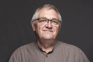 Portrait image of a happy mature man with glasses. Taken on a grey background. 