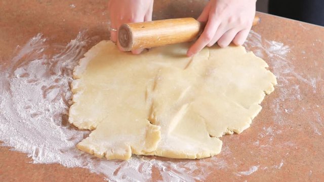 Baker kneading dough with rolling pin on table prepares bread or apple pie