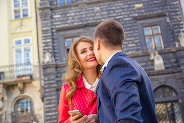 Couple sharing media in a smart phone sitting in bench in park with buildings in the background