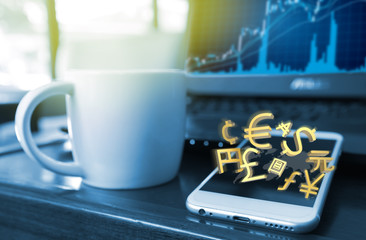 Focus on Golden World currencies sign and blur smartphone screen and laptop stock graph background , flare light