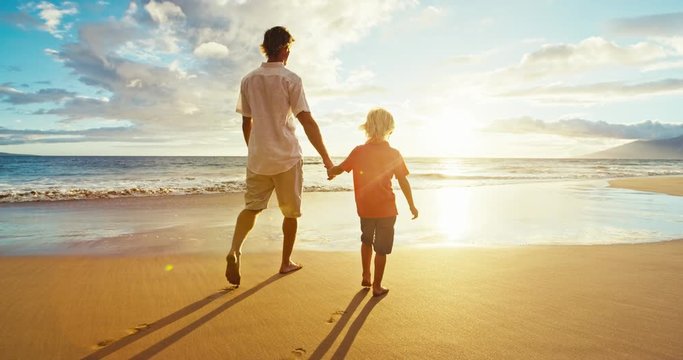 Father and son walking on the beach at sunset