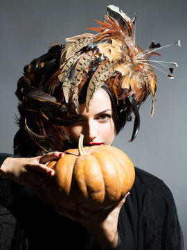 pretty woman in feather hat holds halloween pumpkin