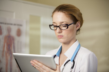 Young beautiful doctor in glasses and white robe using tablet computer. 