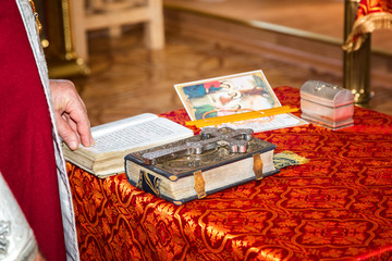 Священник читает Библию. Большой крест лежит на Библию на столе с красной скатертью. На церемонии в христианской церкви.