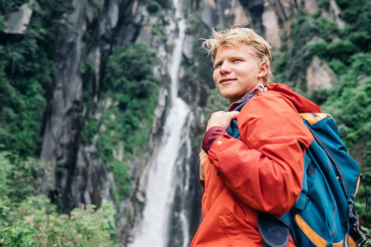 Young man with backpack near the waterfall