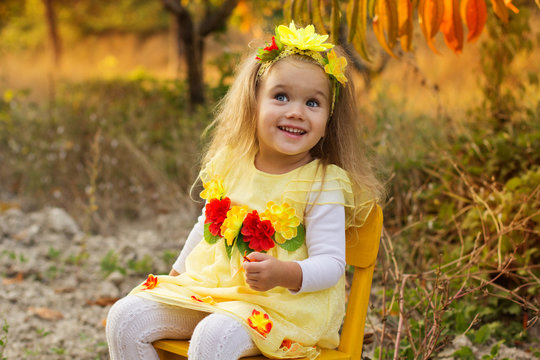 Little girl is sitting on chair in autumn garden